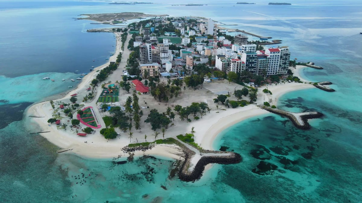 Aerial view of Maafushi Island in the Maldives, showing dense buildings, beaches, and surrounding turquoise lagoon.